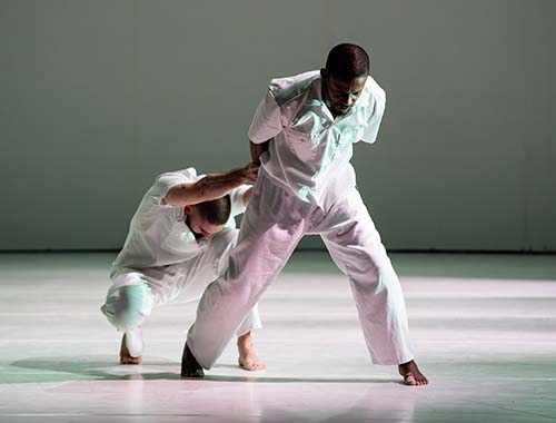Two men in white outfits performing energetically on a stage, engaging the audience with their lively act.