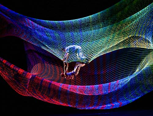 Image of dancers flying high, entangled in a bright, colorful net, creating a playful scene in mid-air.