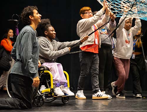 A group of people on stage holding a large net, engaged in a lively performance or demonstration.
