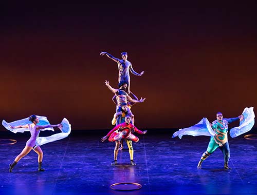 A lively group of dancers performing energetically on stage, showcasing their skills and vibrant costumes.